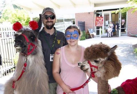 A llama, a principal, a student and an alpaca all smiling outside
