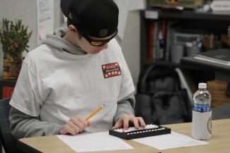 A contestant sits at a desk holding a pencil & uses his abacus to solve an equation during a round of the Abacus Bee