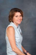 This is a headshot of Anne Baker wearing a blue blouse and a smile.