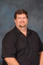 Ed Lukowski, a middle aged man with brown hair and beard wearing a black button down shirt.