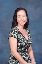 Janet Kurz, woman with black hair and greenish/blue eyes wearing a green and black dress with a slight smile