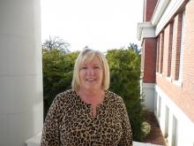 A smiling blonde woman standing in front of several green trees, wearing a brown and black leopard print sweater.