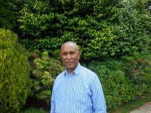 Tesfa Amene, middle age man, shaved hair, has smiling face with deep thought, and green bushes at the background.