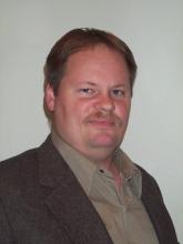 Jeff Bowler, a gentleman with a warm smile, blue eyes, brownish-blonde hair and mustache wearing a brown shirt and jacket.