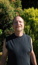 Brian Kindblade, a deaf gentleman with dark brown hair and eyes, with a goatee, wearing a black tank top, smiling.