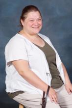 Brooke, a woman in her early 40’s, brown hair pulled back in a ponytail, wearing a white and green shirt, showing her smile.