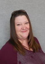 Teresa Phillips a smiling woman in her 40’s with straight, brown, shoulder length hair. Glasses resting on top of head.