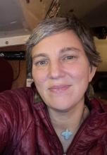 Emily owens, A woman  with short brownish hair wearing a maroon jacket gently smiling at the camera