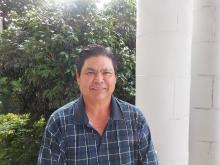 Wayne Oshiro, a guy in front of green plants, blue polo shirt dark hair smiling.