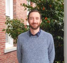 Nicholas is standing outside of the Old Main building smiling.