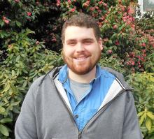 Zach smiling outside of the Old Main building in front of bushes